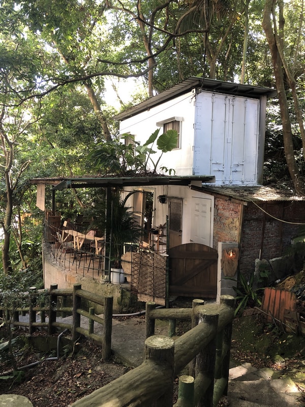 渡深咖啡廳外觀，位於深坑山林中的秘境空間，融合木材、鐵皮與白牆建築，周圍環繞濃密樹林與石階小徑，展現自然靜謐氛圍。