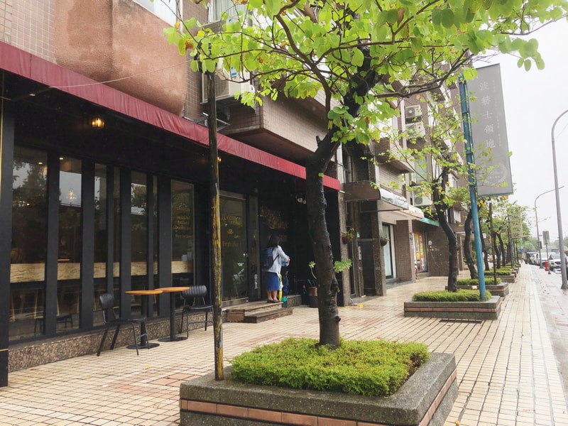 波赫士領地咖啡館明水店，玻璃門面與金色字體交織出靜謐氛圍，綠意點綴街角，彷彿一場文學與感官的邀請。