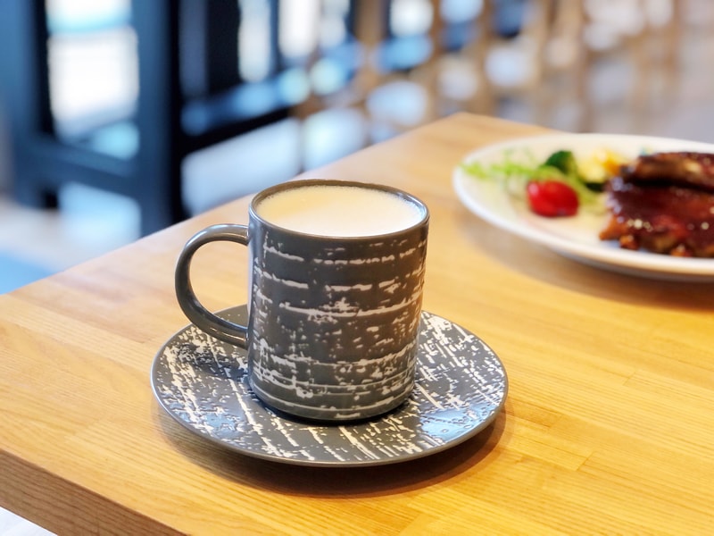 灰白紋理陶瓷杯盛裝英國伯爵鮮奶茶，杯盤相襯如霧中水墨，靜置於溫潤木桌上，背景點綴炙烤肉排與蔬菜，營造靜謐而細膩的午茶時光。